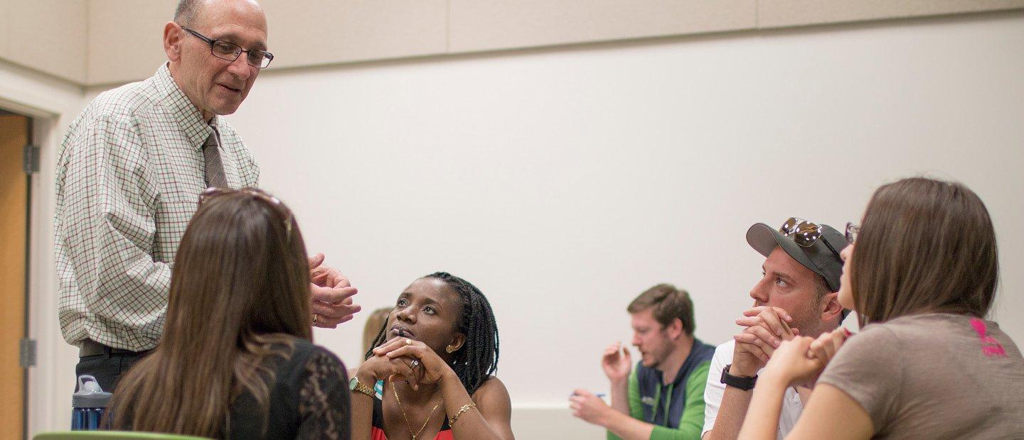 A professor standing next to a table with four students, talking to them.